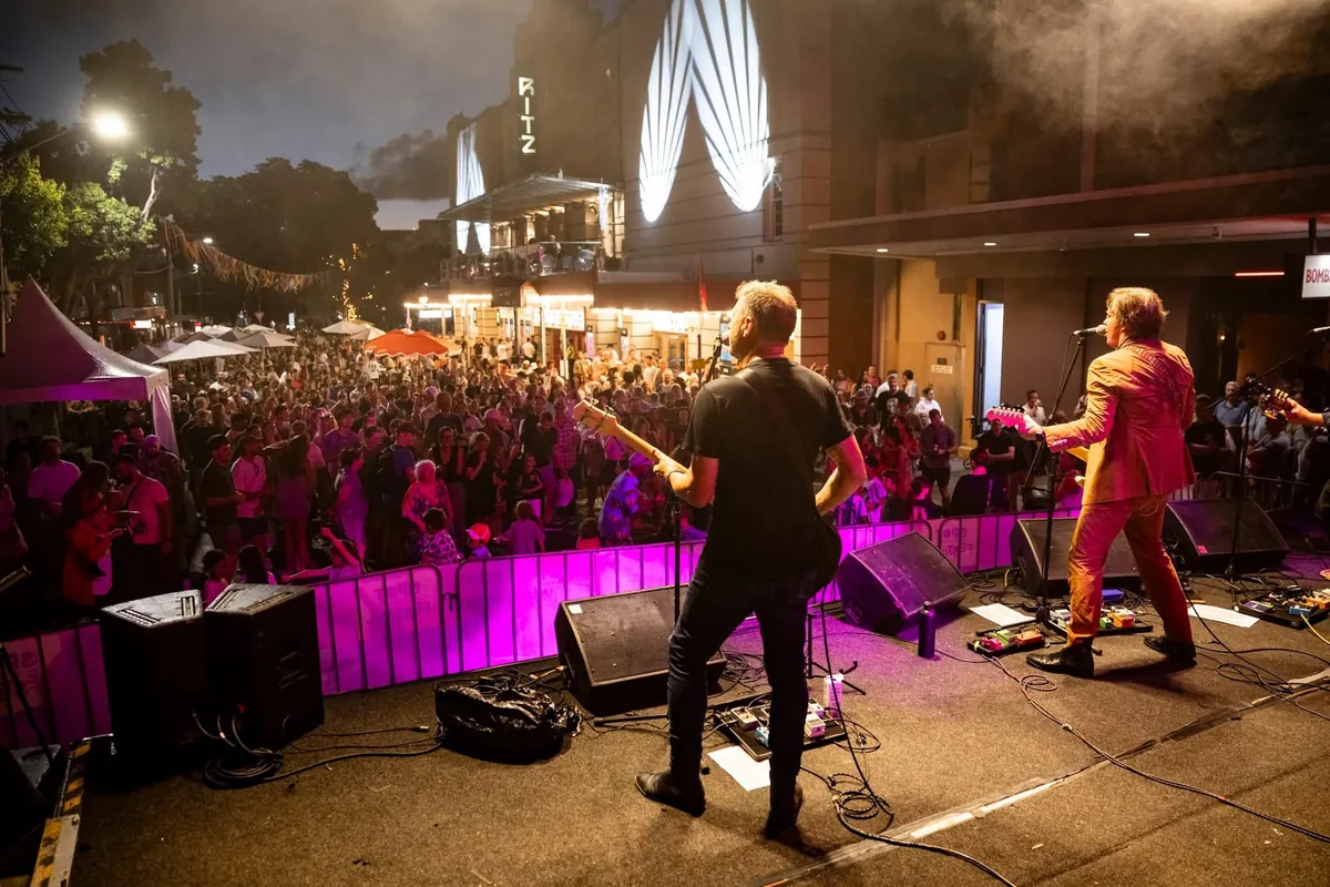A large audience in front of The Pragmatics’ brightly lit outdoor stage at The Spot